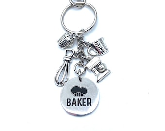 May include: Silver keychain with a round charm that says "BAKER" with a chef hat icon. The charm is attached to a silver ring with a cupcake, measuring cup, whisk, and mixer charms.