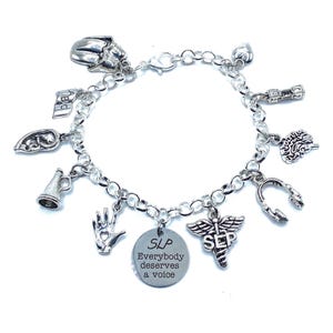 May include: Silver charm bracelet featuring various charms, including a brain, a megaphone, a hand, and a medical symbol. A round charm reads "SLP Everybody deserves a voice". The bracelet is on a white background.