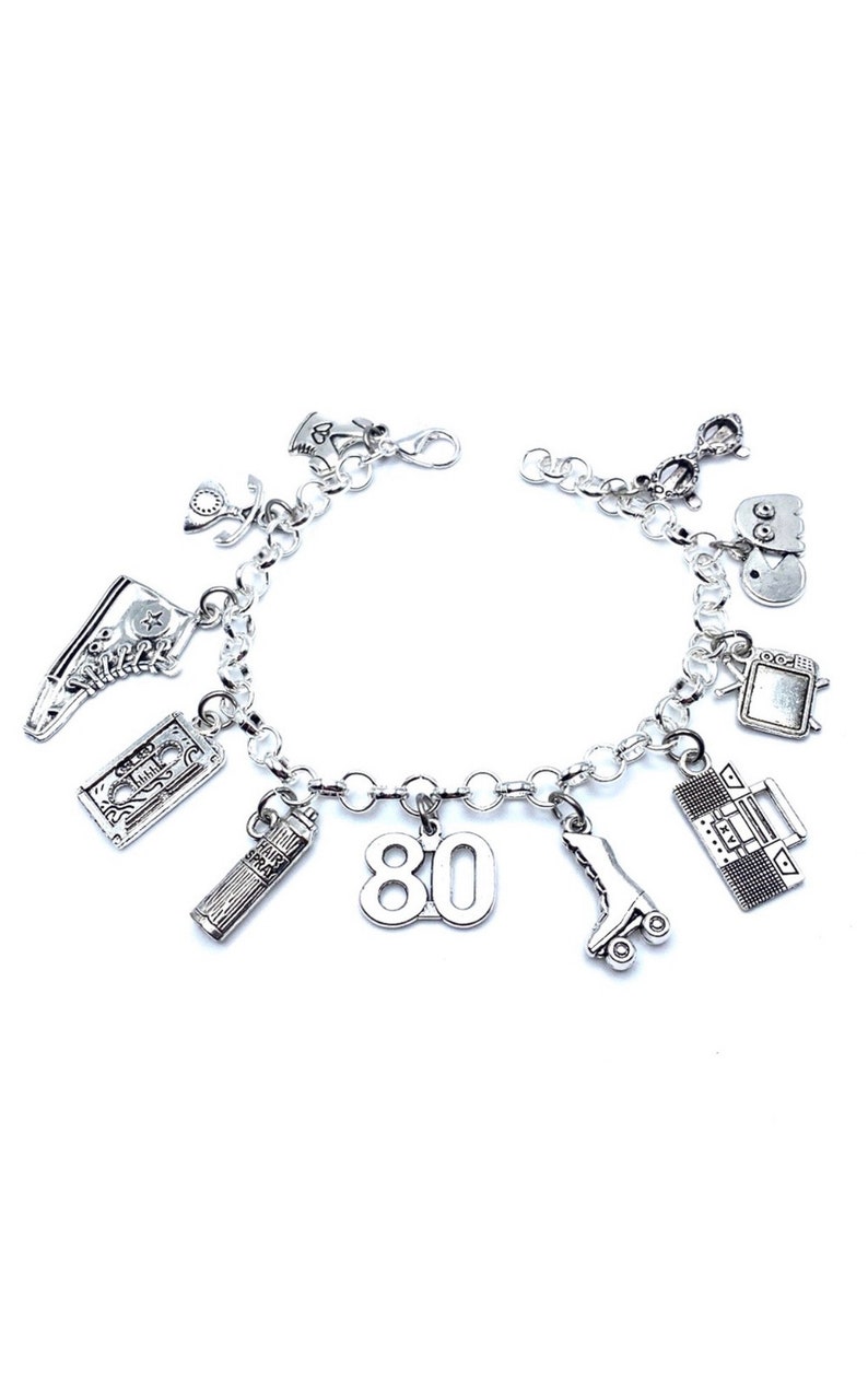 May include: A silver-toned charm bracelet featuring various miniature pendants including a high-top sneaker, a cassette tape, a hairspray can labeled "HAIR SPRAY," the number "80," a roller skate, a boombox, a television, a ghost figure, and glasses.