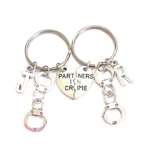 May include: Two silver keychains with a heart charm that says "Partners in Crime" and two silver handcuffs. One keychain has a silver letter "J" and the other has a silver letter "R".