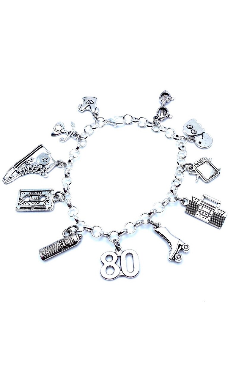 May include: A silver-toned charm bracelet featuring various 1980s-themed pendants, including a high-top sneaker, a cassette tape, a hairspray can, the number 80, a roller skate, a boombox, a television, a smiley face, sunglasses, and a boot.