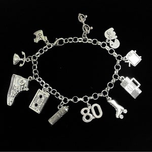 May include: A silver-toned charm bracelet featuring various miniature pendants including a high-top sneaker, a cassette tape, a hairspray can, the number 80, a roller skate, a boombox, a television, a ghost-like figure, glasses, and a telephone.