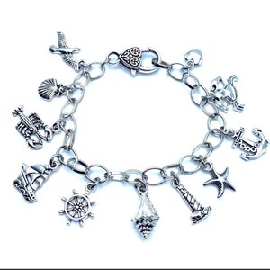 May include: A silver charm bracelet with nautical themed charms, including a sailboat, anchor, seashell, starfish, lighthouse, crab, lobster, and a wheel.