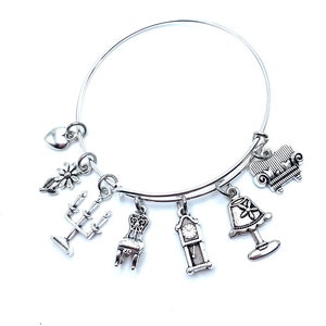 May include: Silver-toned charm bracelet featuring miniature home decor charms. Charms include a sofa, lamp, chair, grandfather clock, and a candelabra. Additional charms include a flower and a heart. The bracelet is on a white background.