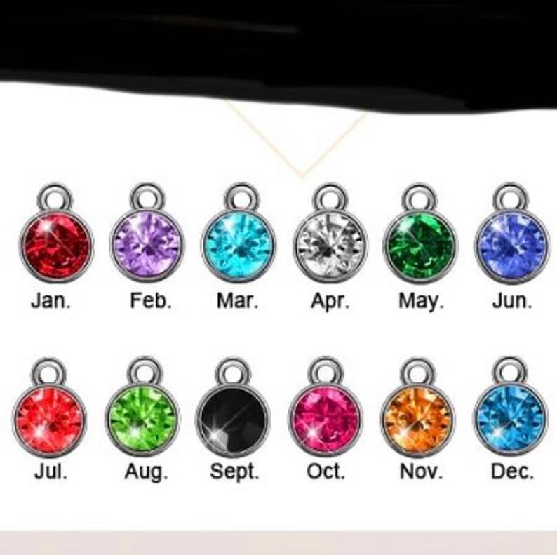 May include: Twelve small charms with different colored rhinestones, each representing a month of the year. January is red, February is purple, March is blue, April is white, May is green, June is light blue, July is red, August is green, September is black, October is pink, November is orange, and December is light blue.