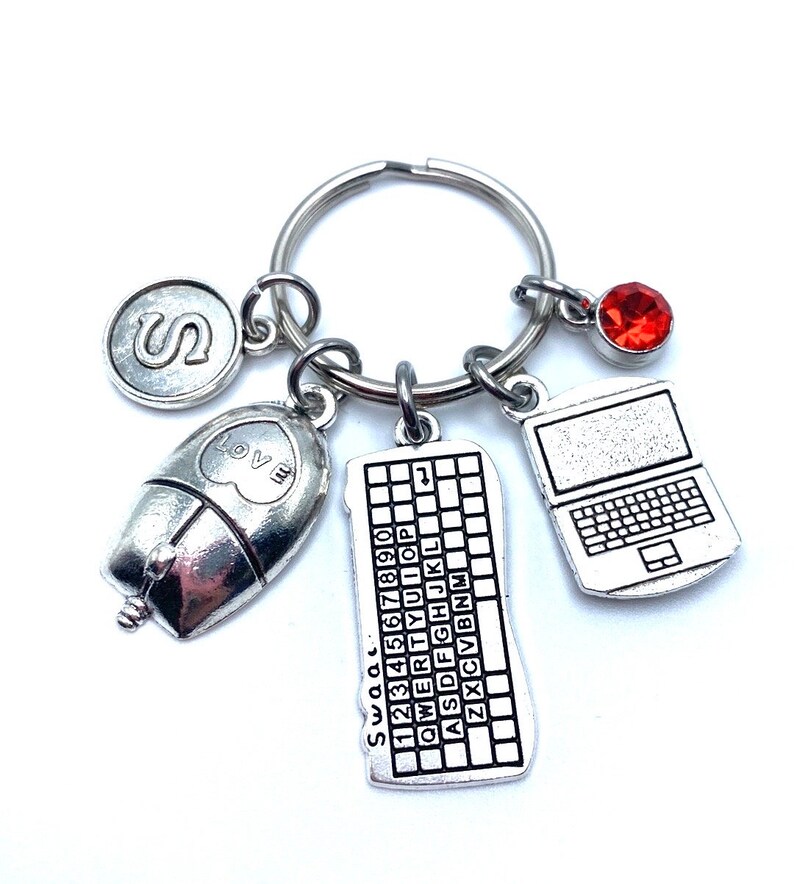 May include: Silver keychain with charms including a computer keyboard, a mouse, a laptop, a red rhinestone, and a charm with the letter "S".