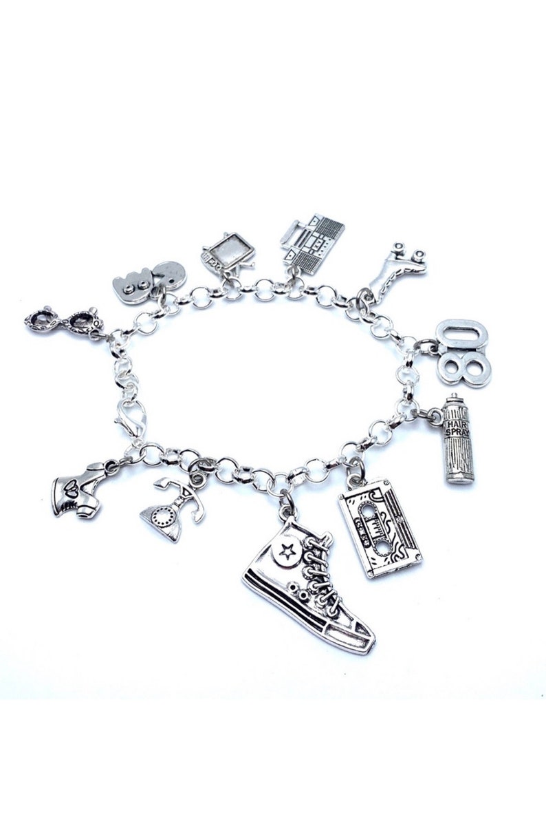 May include: A silver-toned charm bracelet featuring various miniature pendants including a high-top sneaker, a cassette tape, a hairspray can, the number 80, a rotary telephone, roller skates, a boombox, a television, and eyeglasses.