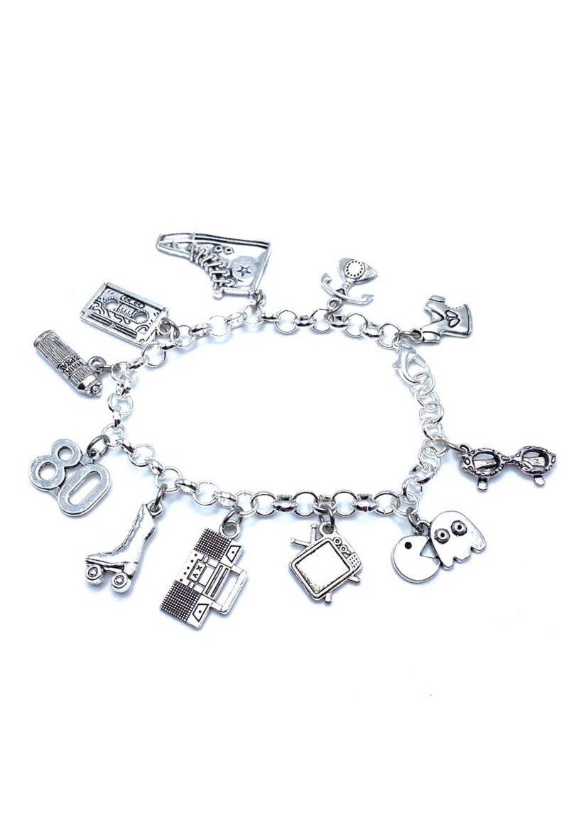 May include: A silver-toned charm bracelet featuring various miniature pendants including a high-top sneaker, cassette tape, hairspray can, the number 80, a roller skate, a boombox, a television, a ghost, a pair of glasses, and a telephone.
