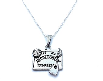 May include: Silver necklace with a silver pendant shaped like a Ouija board. The pendant has the letters "YES" and "NO" at the top, the alphabet, and the numbers 1-8. The pendant also has a sun, moon, and a heart-shaped planchette.