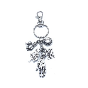 May include: Silver charm keychain with a variety of charms, including a tarot card, a hand, a teacup, and a charm with the words "Success, Money, Happiness".