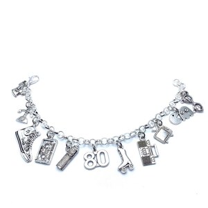 May include: A silver-toned charm bracelet featuring various miniature pendants including a high-top sneaker, a cassette tape, a hairspray bottle, the number 80, a roller skate, a boombox, a television, a ghost character, and a rotary telephone.
