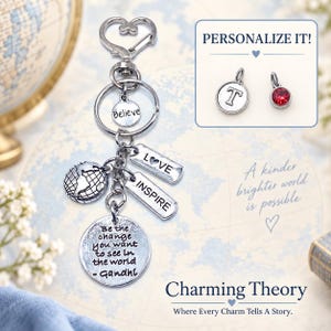 May include: A silver-toned keychain featuring a heart-shaped clasp, a globe charm, and rectangular tags engraved with LOVE and INSPIRE. A round charm displays the text Be the change you want to see in the world - Gandhi, and another says Believe.