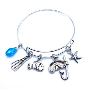 May include: A silver charm bracelet with a blue crystal charm, a fish charm, a scuba mask and snorkel charm, a flipper charm, and a starfish charm.