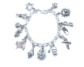 May include: Silver charm bracelet with various beach-themed charms, including a seashell, a sun, a flip-flop, a beach chair, a bucket and shovel, a seagull, and a charm that says "beach girl".