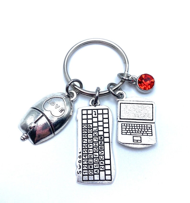 May include: Silver keychain with a computer mouse, keyboard, and laptop charm. The keyboard charm has the letters "Swac" and the numbers "1234567890" printed on it. The laptop charm has a red rhinestone on the top.