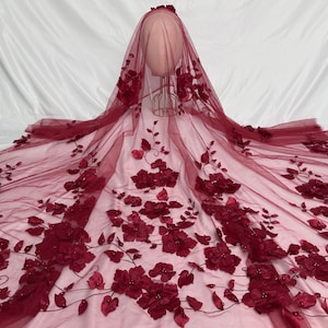 May include: Burgundy floral lace fabric with 3D flowers and leaves. The lace is delicate and intricate, with a soft, flowing texture.