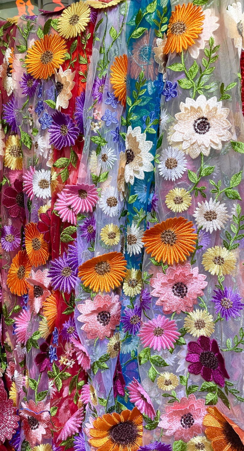 May include: A colorful fabric with embroidered flowers in various shades of pink, purple, orange, and yellow. The fabric has a sheer, mesh-like texture.