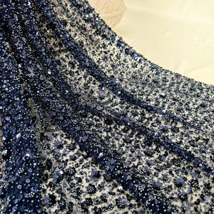 Op de afbeelding: Zwarte parelstof met een delicate mesh-rug. De stof is bedekt met kleine, ronde pailletten die een glinsterend effect creëren.