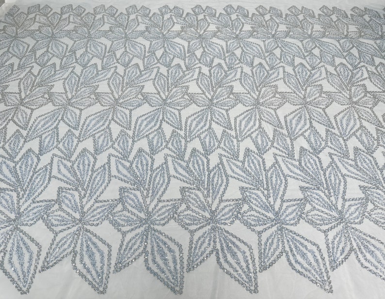 Puede incluir: Tela de cuentas plateadas con un patr&oacute;n floral. La tela tiene un fondo blanco y las flores est&aacute;n hechas de cuentas plateadas.