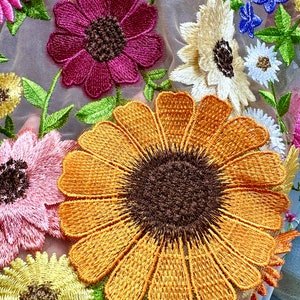 May include: A close-up of a fabric with embroidered flowers. The flowers are in shades of pink, yellow, orange, and blue. The fabric is a sheer mesh.