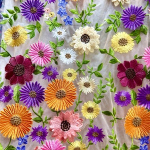 May include: A sheer fabric with embroidered flowers in various colors, including pink, purple, yellow, orange, and red. The flowers are arranged in a random pattern and have a delicate, vintage look.