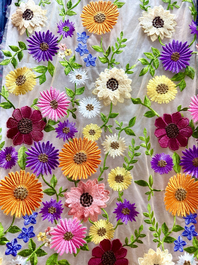 May include: A sheer fabric with embroidered flowers in various colors, including pink, purple, yellow, orange, and red. The flowers are arranged in a random pattern and have a delicate, vintage look.