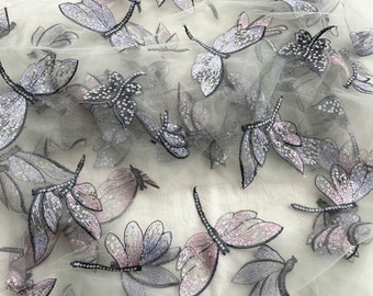以下が含まれることがあります： 刺繍されたトンボのデザインが施された、透き通った白い生地。トンボはスパンコールでできており、薄い紫と銀色の配色になっています。