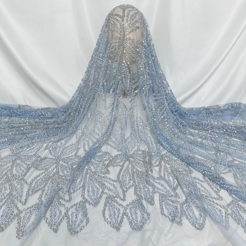 Puede incluir: Tela de encaje azul claro con cuentas y un patr&oacute;n floral. La tela es transparente y tiene un acabado delicado y brillante.