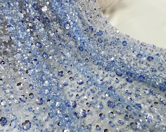May include: Blue and silver sequins on a sheer mesh fabric. The sequins are arranged in a random pattern.