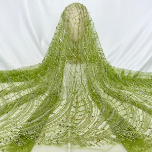 Puede incluir: Tela verde con cuentas y lentejuelas con un patrón geométrico. La tela es transparente y tiene una textura delicada.