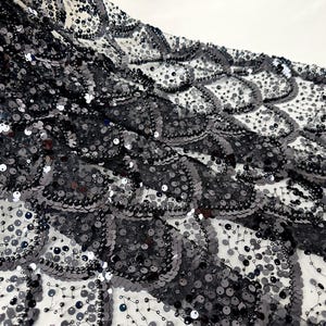 Pode incluir: Close-up de um tecido de lantejoulas pretas com um padrão de escamas. As lantejoulas são em vários tons de cinza e preto, criando um efeito texturizado e brilhante. O tecido é provavelmente usado para roupa de noite ou fins decorativos.