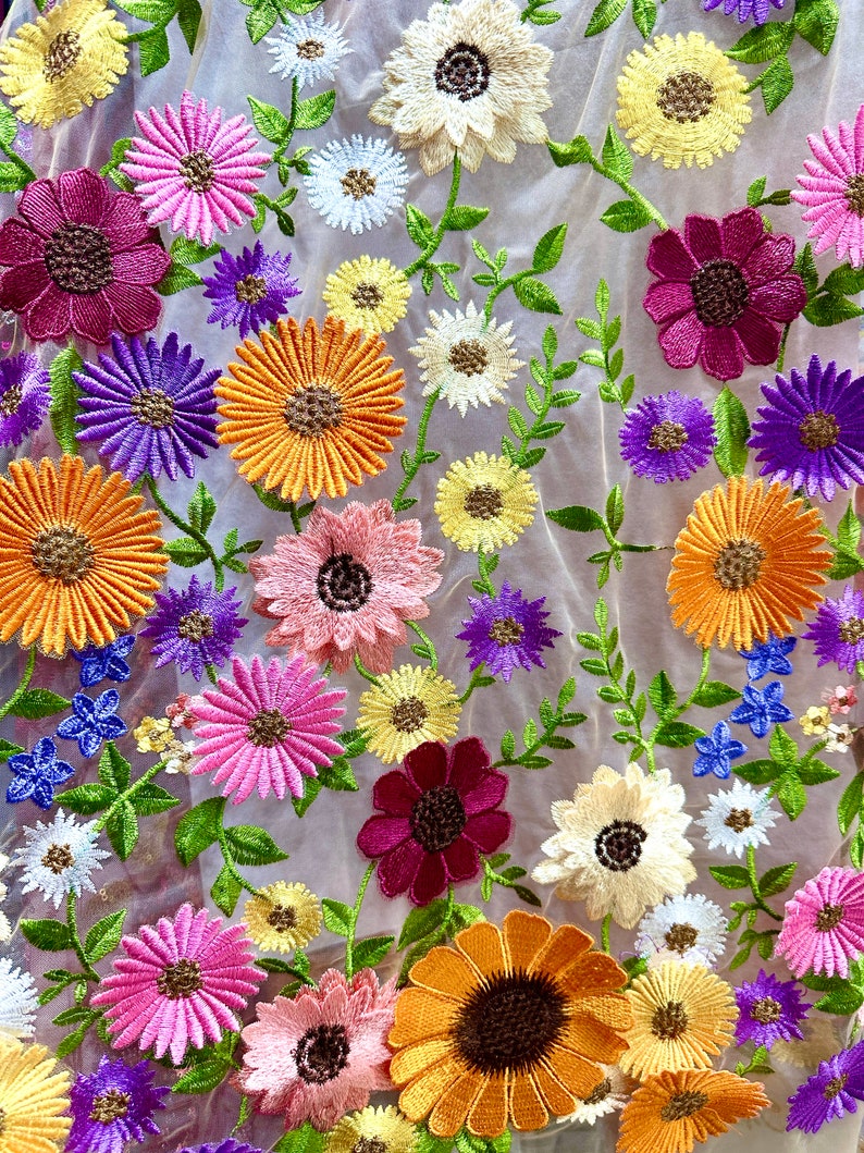 May include: A sheer fabric with embroidered flowers in various colors, including pink, purple, orange, yellow, and red. The flowers are arranged in a random pattern and have a delicate, vintage look.