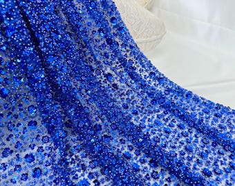 Puede incluir: Tela azul real con cuentas y un delicado patrón floral. La tela está hecha de un material de malla transparente y está adornada con pequeñas lentejuelas brillantes.