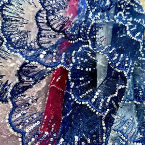 May include: Close-up of a navy blue lace fabric with silver sequins. The fabric has a delicate floral pattern and is ideal for crafting or sewing projects.