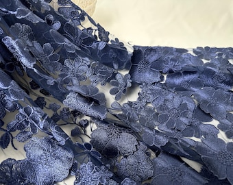 May include: Close-up of navy blue floral embroidered fabric. The fabric features detailed, raised floral patterns with a delicate, sheer background. The flowers are densely packed, creating a textured, elegant look, suitable for apparel or decor.
