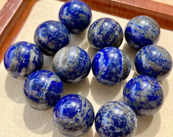 May include: A collection of twelve smooth, round, blue lapis lazuli gemstone spheres. The spheres are arranged in a circle on a white surface.