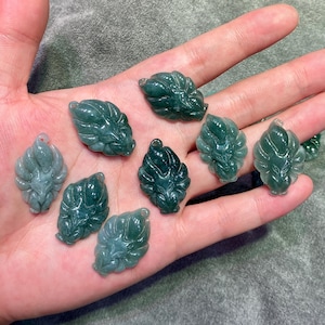 May include: A collection of jade pendants in the shape of stylized leaves. The pendants are various shades of green, with intricate carved details. Each pendant has a small hole for stringing.