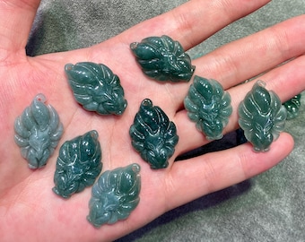 May include: A collection of jade pendants in the shape of stylized leaves. The pendants are various shades of green, with intricate carved details. Each pendant has a small hole for stringing.