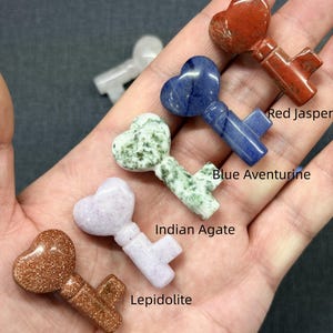 Op de afbeelding: Een verzameling edelstenen sleutelhangers, elk met een hartvormige bovenkant. De sleutels zijn gemaakt van Golden Sandstone, Lepidoliet, Indian Agate, Blue Aventurine en Red Jasper. De hangers worden gepresenteerd op een donkergrijze ondergrond.