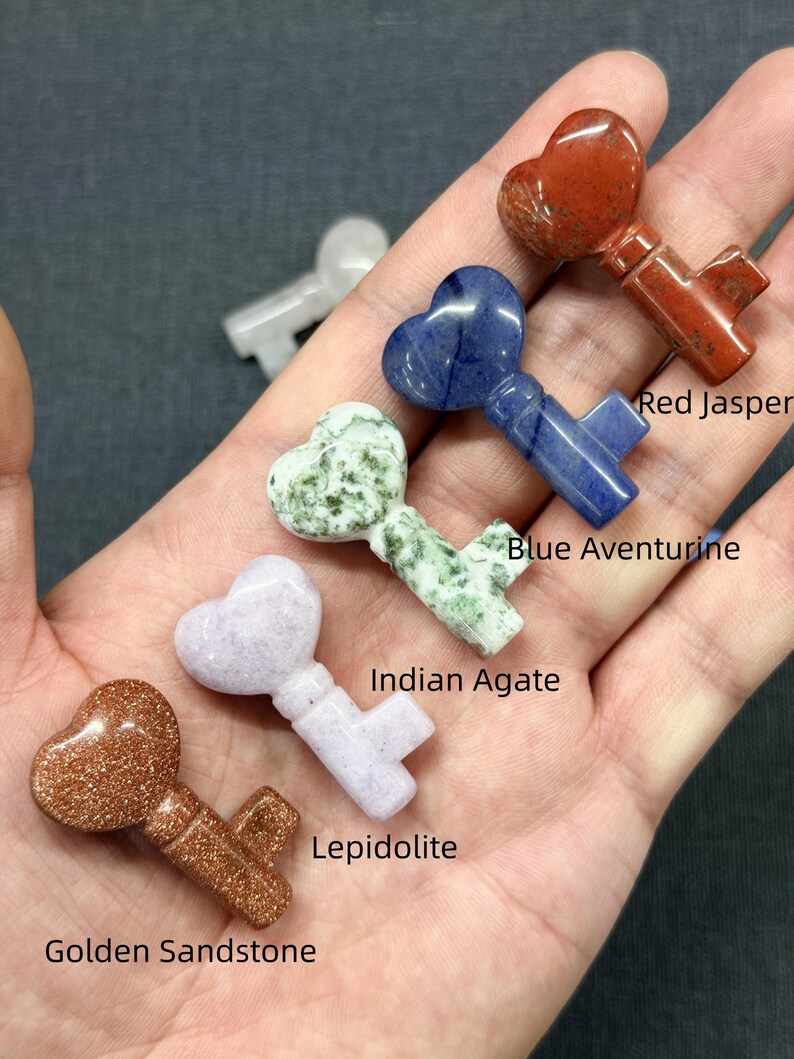 Op de afbeelding: Een verzameling edelstenen sleutelhangers, elk met een hartvormige bovenkant. De sleutels zijn gemaakt van Golden Sandstone, Lepidoliet, Indian Agate, Blue Aventurine en Red Jasper. De hangers worden gepresenteerd op een donkergrijze ondergrond.