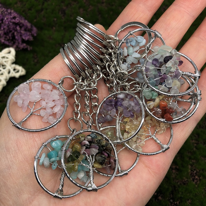 May include: A set of colorful gemstone tree of life keychains. Each keychain features a silver wire tree with a variety of gemstones, including pink, purple, green, blue, and red.