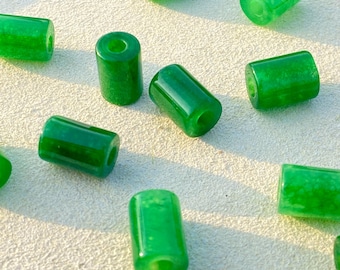 May include: A collection of bright green, cylindrical beads with a polished, glossy finish. Each bead has a hole running through the center, and they are scattered across a light-colored surface. The beads are approximately 0.5 inches in length.