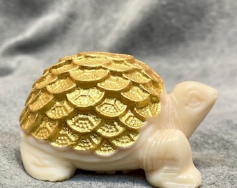 May include: A decorative turtle figurine with a cream-colored body and a gold-colored shell. The shell has a textured, scale-like pattern. The figurine is a small, detailed sculpture.