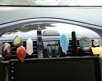 May include: A collection of colorful crystal and gemstone car air vent clips. The clips include a purple fluorite, a pink rose quartz, a green labradorite, a red carnelian, a blue feather, a black obsidian, a grey labradorite owl, and a yellow citrine.