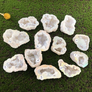 May include: Twelve iridescent white agate geode slices with numbers 1 through 25 written on them. The geode slices are arranged in a circle on a green surface.