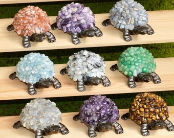 May include: A collection of decorative stone turtle figurines. Each turtle features a shell made of colorful, small stones in shades of orange, purple, blue, white, and green. The turtles have dark gray bodies and legs, and are displayed on wooden shelves.