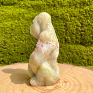 May include: A green, white, and brown carved onyx gorilla figurine. The gorilla is sitting with its arms crossed and its head tilted to the side.