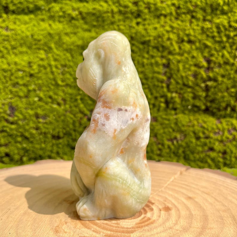 May include: A green, white, and brown carved onyx gorilla figurine. The gorilla is sitting with its arms crossed and its head tilted to the side.