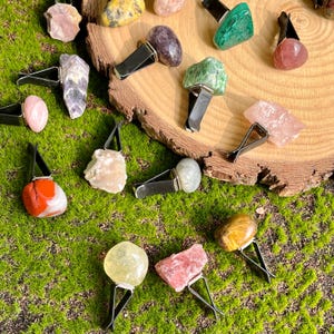 May include: Assortment of colourful crystal car air fresheners. The crystals are attached to black metal clips. The crystals are displayed on a wooden surface and a green mossy surface.