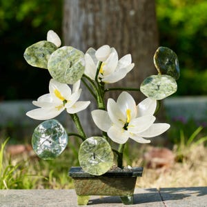 Puede incluir: Una escultura de flor de loto de piedra verde jade y blanca en una maceta verde jade. La escultura presenta múltiples flores y hojas de loto.